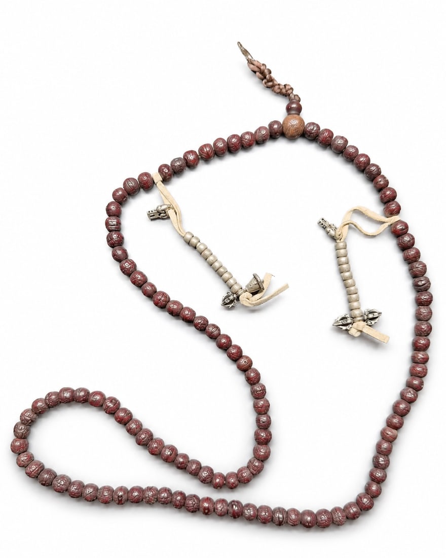 Tibetan 108-Bead Mala with Metal Counters, Described as Phoenix-Eye Bodhi, Qing Dynasty: A Tibetan Buddhist mala described by the owner as comprising 108 phoenix-eye bodhi beads, with dark reddish-brown surfaces, a lustrous finish, and varied surface markings. The strand includes a larger