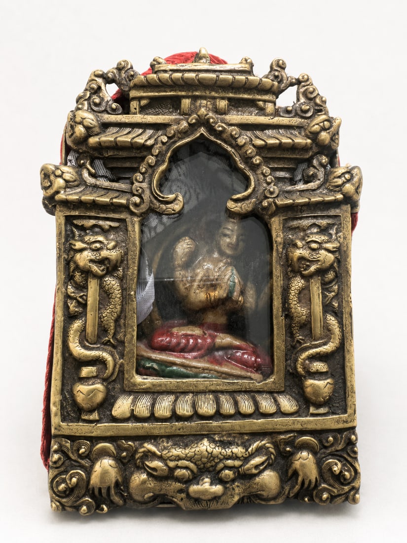 Tibetan Gau Shrine with a Ceramic Figure of Four-Armed Avalokiteshvara: A Tibetan portable shrine, or gau, with an architectural metal front featuring tiered eaves, paired dragon motifs and a beast-mask ornament beneath the glazed opening. The interior houses a polychrome