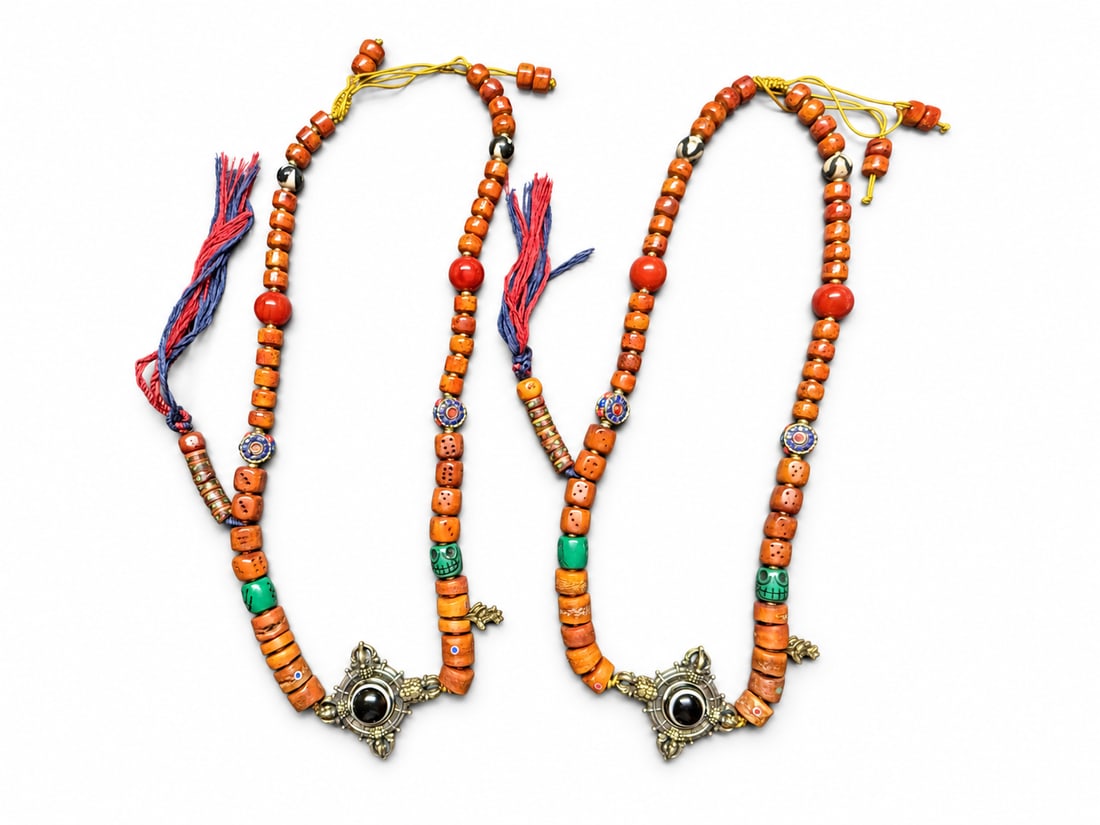 Pair of Himalayan Medicine Buddha Beans Neckless with Black-and-White Pendants: A coordinated pair of Himalayan-style beaded necklaces, each featuring a black-and-white medicine-bead-style centerpiece within an ornamental metal mount. Orange barrel and disc beads are interspersed