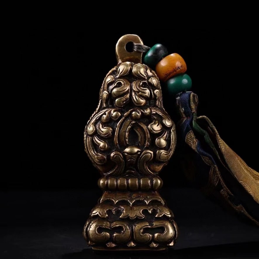 Tibetan Seal with Three Beads and Textile Tie, Qing Dynasty: A Tibetan seal accompanied by three Tibetan beads and a patterned textile tie, described by the owner as old. The shaped metal handle is richly decorated with raised scrolling foliage and bud-like mot