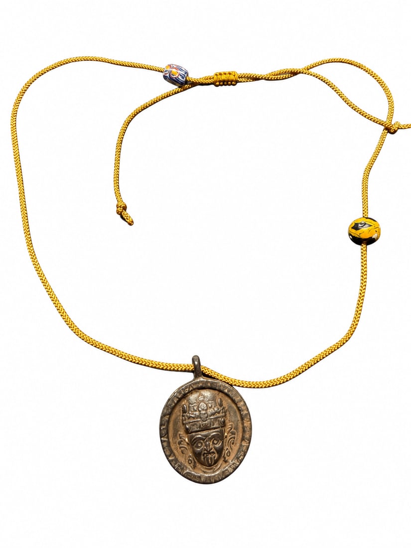 Qing Dynasty, Tibetan Amulet Depicting a Deity, Possibly Zakiram: A Tibetan devotional amulet, possibly depicting Zakiram, the female wealth deity, Qing dynasty. The front features a crowned face in relief with wide eyes and a protruding tongue, framed by a border o