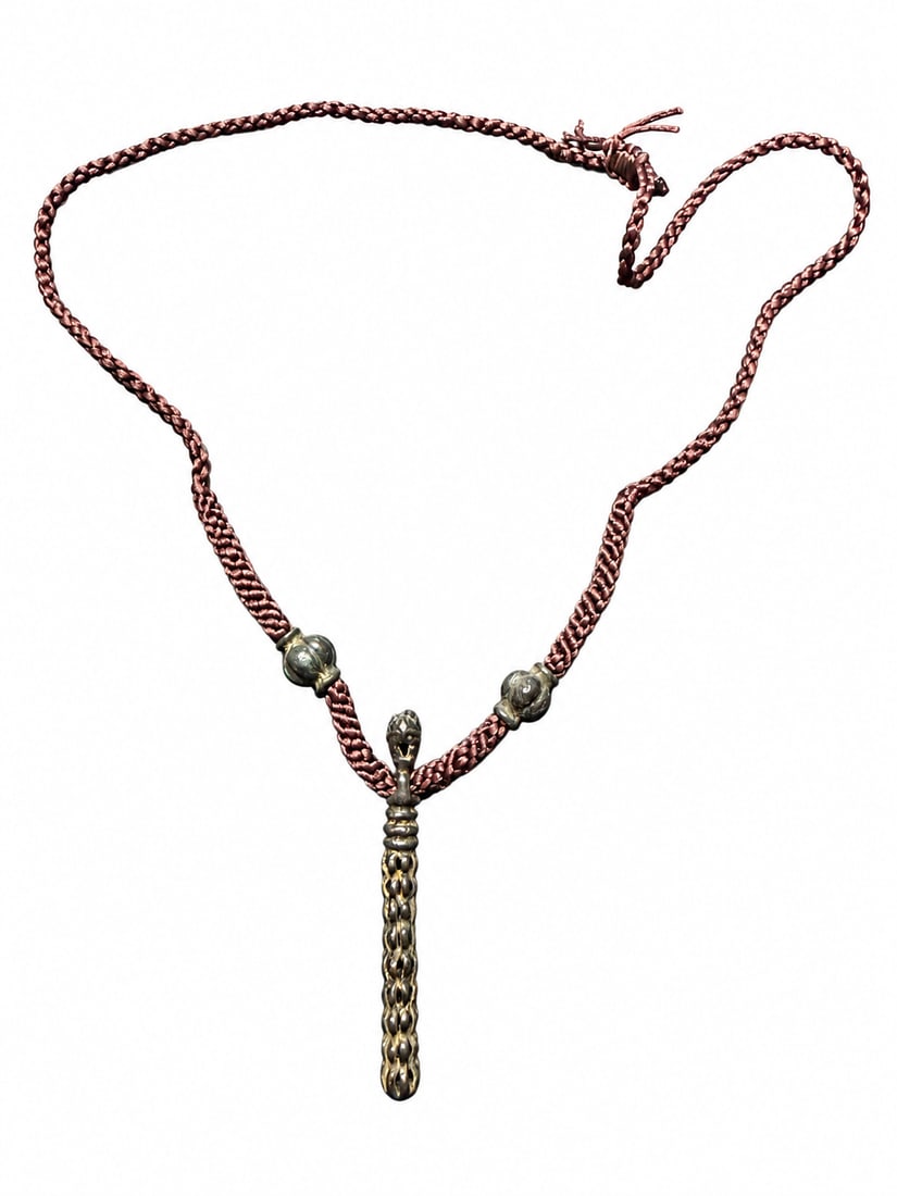 Yuan or Ming Dynasty, Tibetan Miniature Buddhist Staff-Form Amulet: A Tibetan miniature Buddhist staff-form amulet with a sculpted mask-like terminal, ringed neck and an elongated body decorated with repeated petal-like forms and narrow openings. The metal surface dis