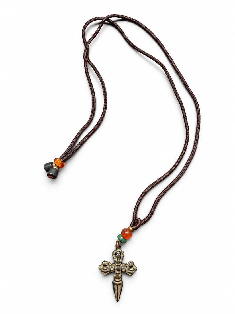 Yuan or Ming Dynasty, A Tibetan miniature Buddhist staff-form amulet with a sculpted mask-like termi: A miniature Tibetan crossed-vajra-form amulet combining three vajra terminals with a tapered, phurba-like lower point. Despite its small size, the pendant displays detailed lotus-petal collars, a rais