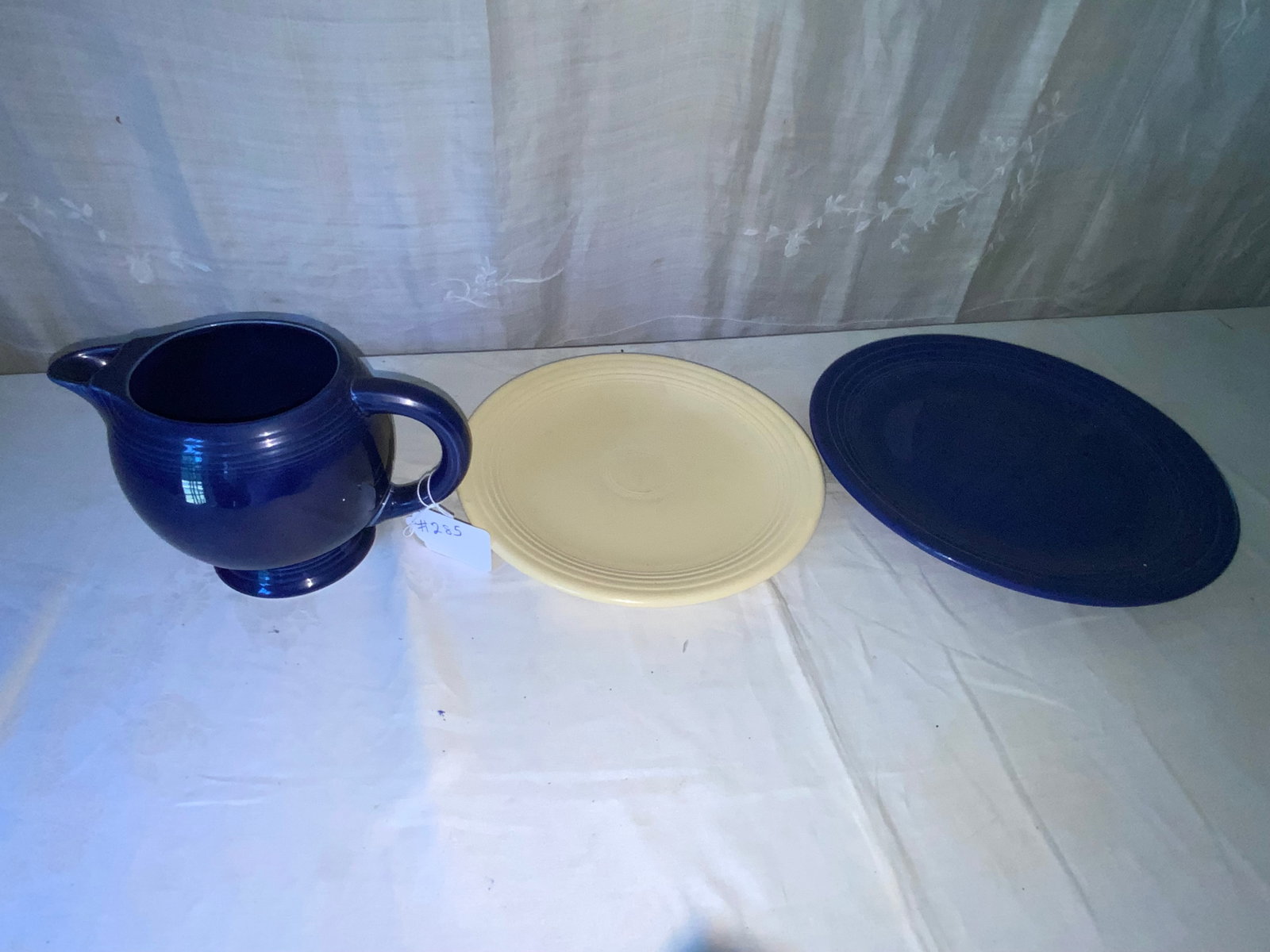 Fiesta Pitcher & Platters: Fiesta: blue pitcher 6 1/2" round by 6 1/2" tall, blue platter 14 1/2" oval, ivory platter 12 1/2" round. Good condition.