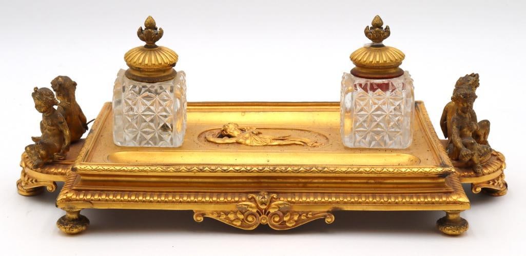 Elkington & Co. Cherub Gilt Bronze & Crystal Double Inkwell: Elkington & Co. (British, est. 1836) Cherub Figural Double Inkwell Gilt bronze with cut crystal inkwells Elaborate desk inkwell featuring a rectangular gilt bronze base richly decorated with class