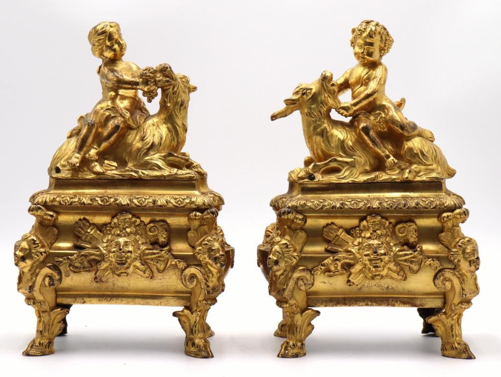 French 18th C. Régence Gilt-Bronze Chenets: French Régence Gilt-Bronze Chenets First Quarter 18th Century Pair of gilt-bronze chenets, each depicting a child seated astride a goat. Raised on shaped bases applied with Bacchic masks, ramR