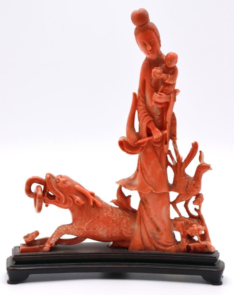 Chinese Carved Coral Sculpture of Guanyin, Mythical Creatures: Chinese Guanyin with Child and Mythical Creatures Carved coral sculpture on wooden stand Elaborately carved coral figural group depicting Guanyin holding a child, accompanied by a recumbent dragon-lik