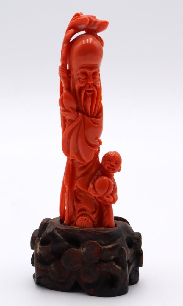 Chinese Carved Coral Immortal with Child Sculpture: Chinese Immortal with Child Carved coral sculpture on wooden stand Carved coral figural group depicting a bearded Chinese immortal accompanied by a child holding a peach, with an animal modeled above 