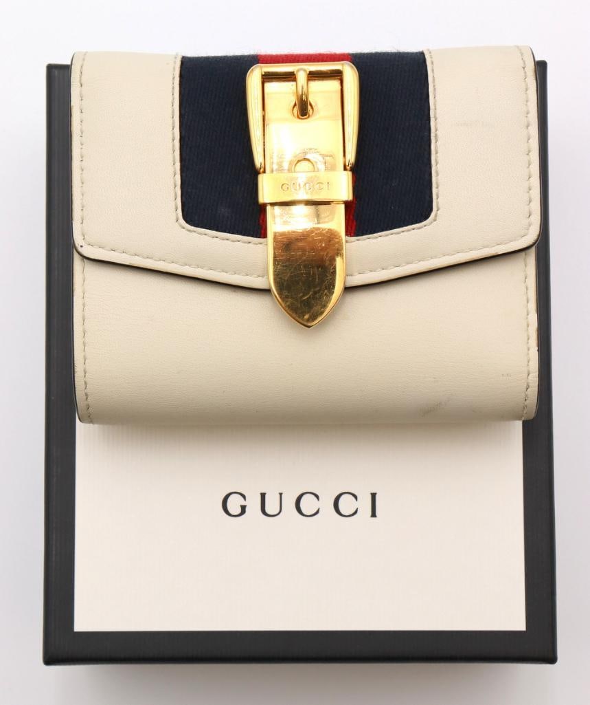 Gucci Sylvie White and Gold Tri-Fold Wallet: Gucci (Italian, est. 1921) Sylvie Tri-Fold Wallet White leather with Web stripe and gold-tone hardware Gucci Sylvie tri-fold wallet crafted in white leather with the house’s signature Web stripe