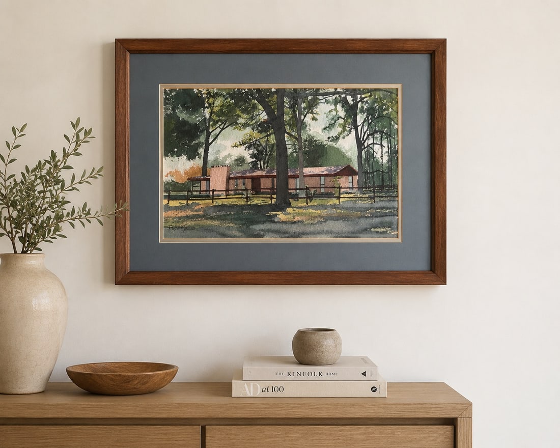 Mid-Century Modern House Watercolor Painting: A watercolor painting depicting a mid-century modern style house nestled amongst trees with a fence in the foreground, presented in a wooden frame with a grey mat.