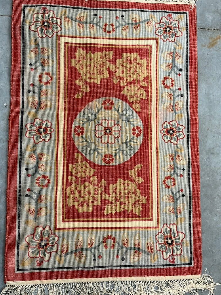 Handcrafted Oriental Rug with Floral Patterns: "Handcrafted Oriental Rug with Floral PatternsThis elegant rug features a rich red background with intricate floral designs in gold, blue, and black, and includes decorative fringe."