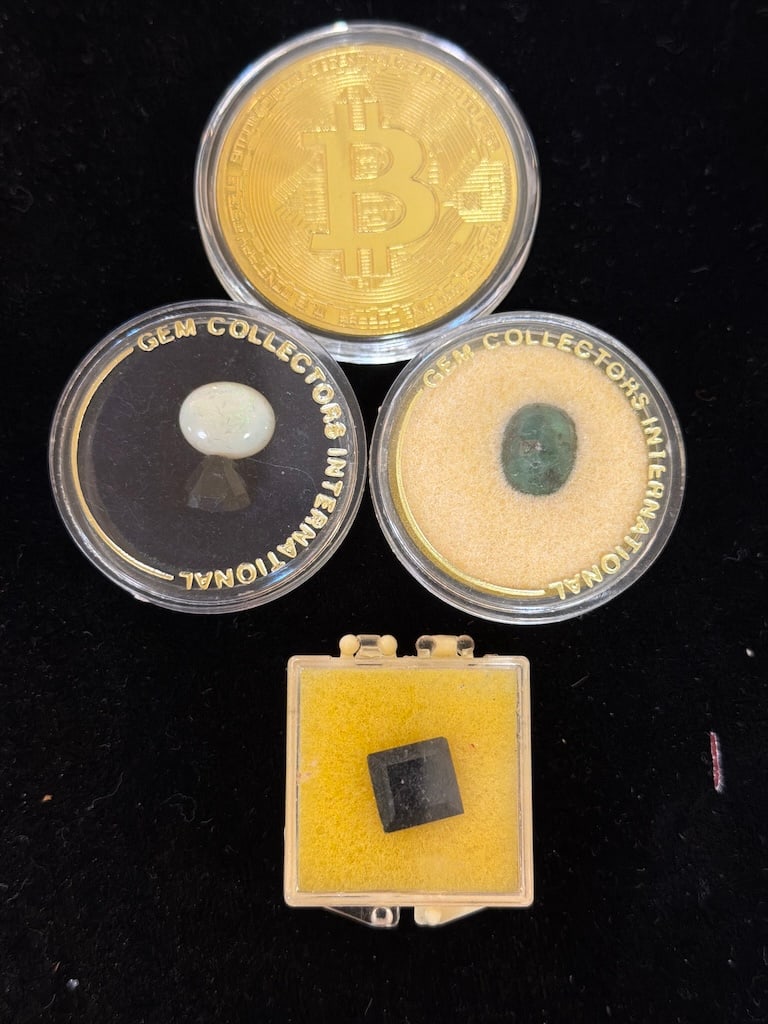 Collection of Gemstones and Bitcoin Coin: "Collection of Gemstones and Bitcoin CoinThis auction features a Bitcoin token, an white gemstone, a green gemstone, and a black mineral, all displayed in protective cases."