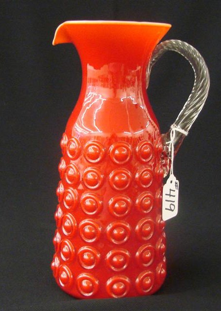 Art Glass Pitcher with Red Exterior & Salmon Cased: Cased Art Glass Pitcher with Red Exterior & Salmon Interior with Embossed Bullseye Pattern and Applied Clear Twist Handle. Possible Michael & Frances Higgins. Auction Estimate $100-200.
