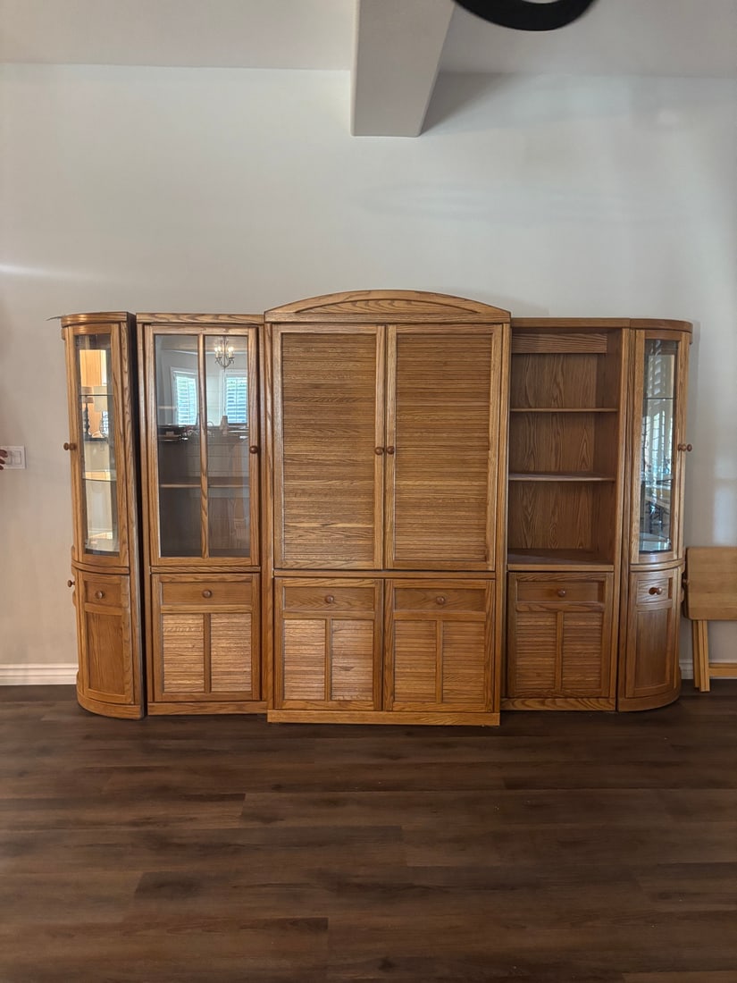 5-Piece Oak Entertainment Wall Unit: Five-piece oak wall unit with center TV cabinet with louvered double doors and arched top, flanked by two glass-door curio cabinets and two curved corner cabinets with glass fronts. Base cabinets have