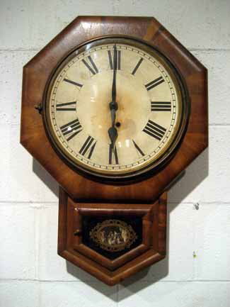 Antique Ansonia Walnut Key Wind Cased Wall Clock: Ansonia short drop walnut cased wall clock with lower glass paneled door, original label CONDITION: not in running condition SIZE: 25" high, 17" wide