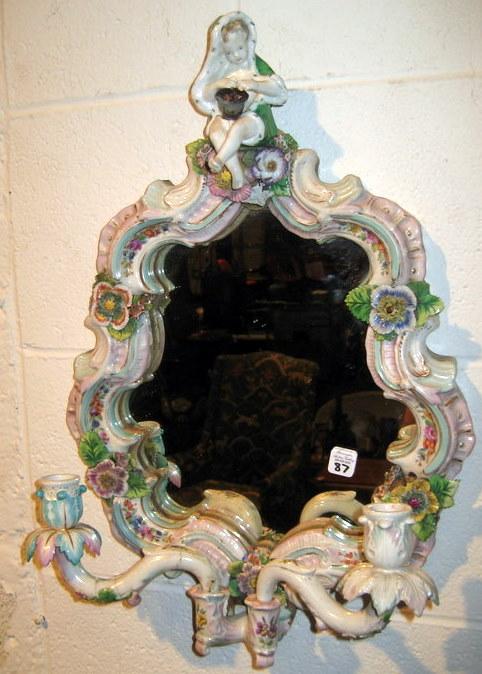 Capodimonte Style Wall Mirror: Capodimonte style wall mirror decorated with young child at crest and two candle holders - damage to one candle holder and applied flowers on frame, 18.5" high, 12.5" wide. Age: antique.