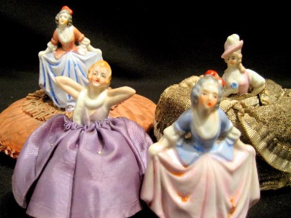 2 Porcelain Half Dolls: Two porcelain half dolls, both with pin cushion bases and two porcelain figures of ladies holding skirts, one with pin cushion base.