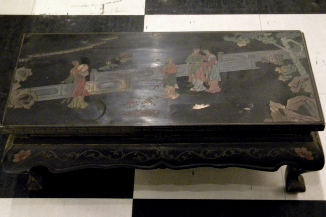 Black Lacquer Footstool dec/w Geisha in Garden Scene: Black lacquer footstool decorated with Geisha in garden scene, 9" high, 24" wide - some damage to top.