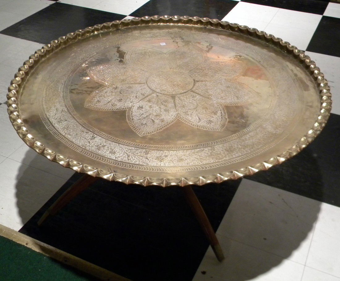 Lrg Round Brass Coffee Table on Wooden Stand: Large round brass coffee table decorated with central flower motif and pie crust edge on foldable wooden stand, 18"high, 42" diameter overall