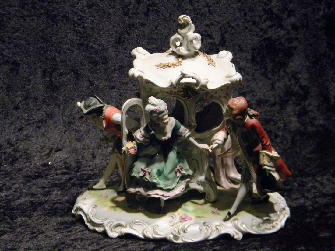 Meissen style glazed porcelain figural group: Meissen style glazed porcelain figural group: lady in green dress descending from sedan chair and two coachmen in red coats and tri-point hats, applied flowers to base, marked on base crossed swords,