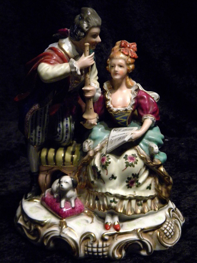 Dresden Style Glazed Porcelain Figural Group: Dresden style glazed porcelain figural group: seated woman holding sheet music, man hold wind instrument while kneeling on stool and dog laying on pillow, marked in black made in Occupied Japan,9.5" h