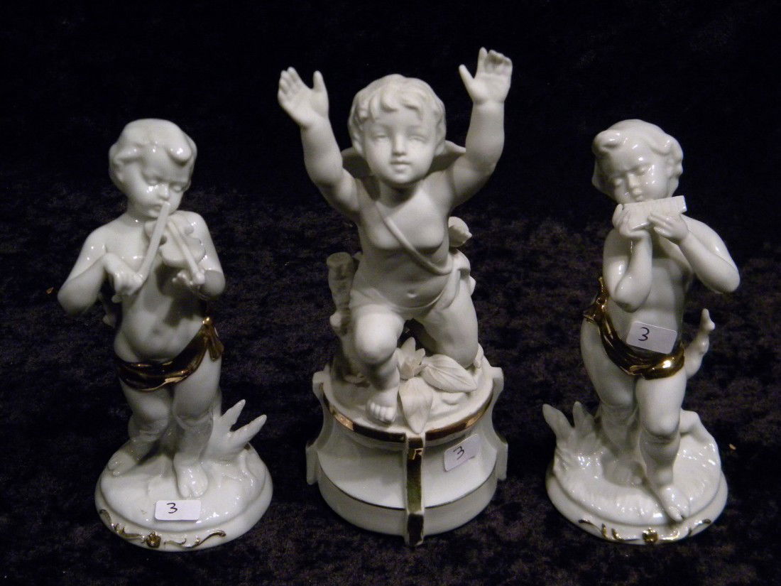 3 White Porcelain Figurines: Three white porcelain figurines: pair glazed, one with flute (missing finger) and one with violin - damaged, both 6" high and white bisque porcelain cherub with bow and arrow, 7.5" high - arm repaired