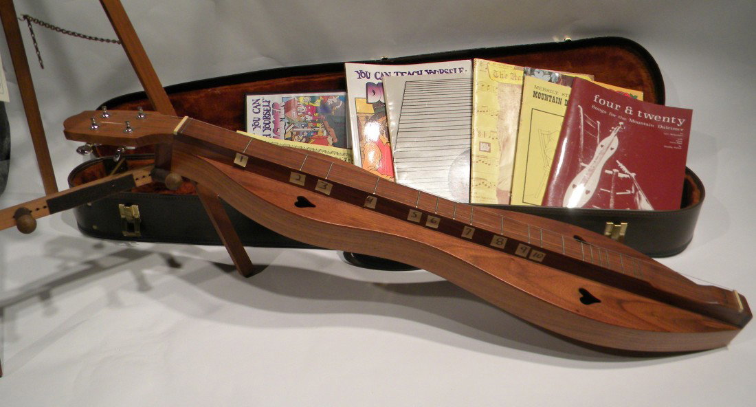 McSpadden Mountain Dulcimer: McSpadden Mountain Dulcimer (36" long) with wooden display stand and 6 "How to Play" Instruction music books and Video. Tag reads Feb 1998 Model SSW. Made in Mt. View, Arkansas, signed George Looney. 