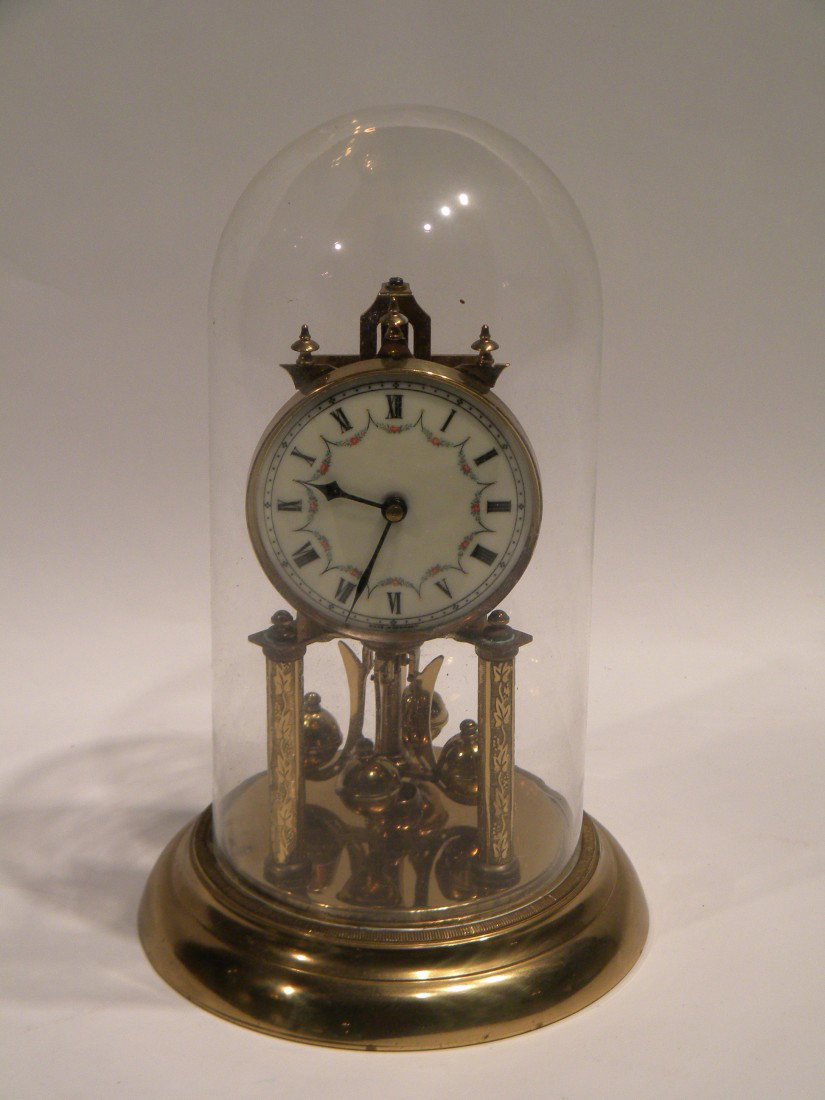 German Brass Anniversary Clock Under Glass Dome: German brass anniversary clock under glass dome, porcelain dial with Roman Numerals and painted roses, marked made in Germany, clock 10" high. Works marked on back "Jahresuhrenfabrik 49" Germany. No (