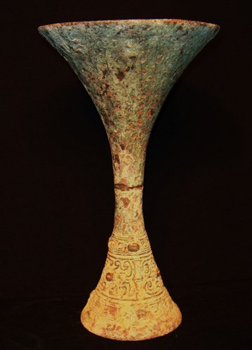 A SMALL ARCHAIC BRONZE WINE VESSEL, GU,LATE SHANG D: the long trumpet neck with a flared mouth, with a slender band of taotie masks encircling the waist 9''H