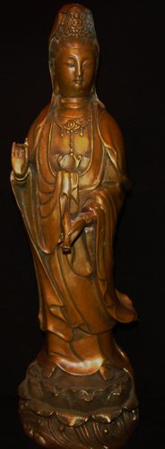 A BRONZE FIGURE OF GUANYIN 19 CENTURY: the deity standing upon a lotus plinth, serenely gazing down, draped in a flowing robe sweeping to her right, the left hand at her chest holding an amphora vase, the right hand bent at the elbow with