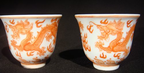 A PAIR OF IRON-RED AND UNDERGLAZE-BLUE-DECORATED C: Each of bell shape, finely painted in iron red with two dragons racing above a band of foam-flecked waves and separated by cruciform clouds, between double blue line borders2 3/8 in. (6 cm.) diam. (2)