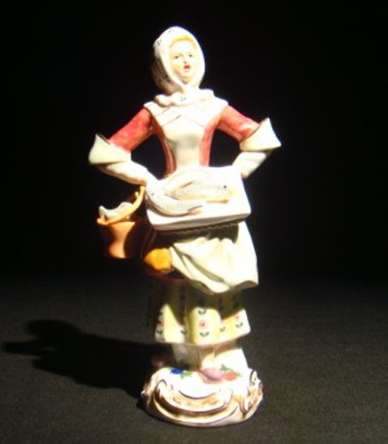 A Meissen porcelain figure of a female fishmonger: A Meissen porcelain figure of a female fishmonger, a tray of fish at her hip, a basket of fish in hand. Cross swords mark in blue under glaze, Incised mark, "11," impressed mark, "132." . 8"H, Circa -