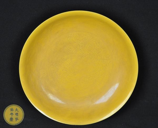 A YELLOW GROUND ANHUA DISH.(MARK AND PERIOD OF HON: Carved with two dragons chasing a pearl six character marks on the base. 8 1/2'' diam