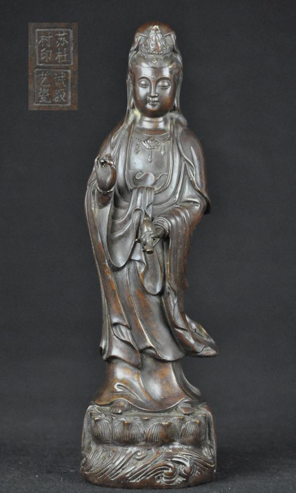 A BRONZE FIGURE OF GUANYIN .(QING DYNASTY): Shown standing with one hand holding a vase, wearing long flowing robes and a cowl finely inlaid in silver, the hair drawn up into a topknot behind a crown, with bead urna and beads in the necklace an
