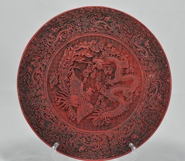 A CINNABAR LACQUER DISH.(QING DYNASTY): The interior is decorated with dragons and phoenixes surrounded with clouds, the exterior is decorated with plum, bamboo, and rocks. 12-1/2 diam.