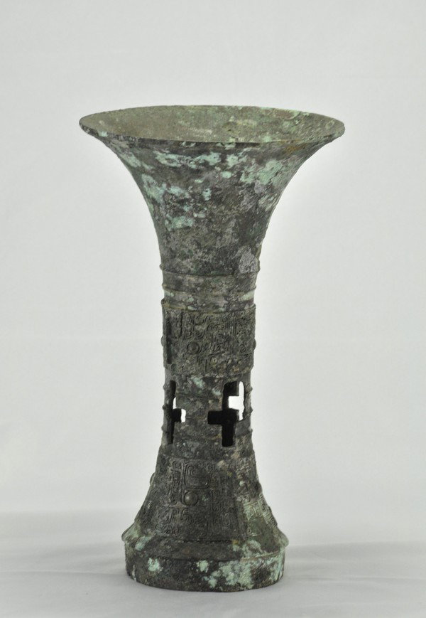 AN ARCHAIC BRONZE RITUAL FOOD VESSEL (GU) (SHANG): the straight central section and gently flared foot both similarly decorated with taotie masks assembled from isolated raised elements on a fine leiwen ground and bisected by notched flanges, the surf