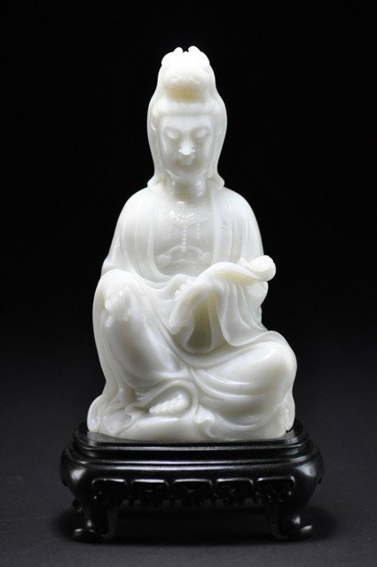 A SOAPSTONE FIGURE OF GUANYIN.(BAIFURONG): Modelled seated with one leg crossed in front of the other, exposing the bare foot, one hand resting on a raised knee whilst the other is holding ruyi, raised at waist level, dressed in a voluminous r