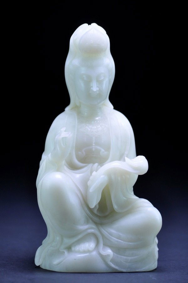 A WHITE JADE CARVING OF GUANYIN.: A WHITE JADE CARVING OF GUANYIN. Modelled seated with one leg crossed in front of the other,exposing the bare foot,one hand is holding ruyi,raised at waist level,dressed in a voluminous robe falling i
