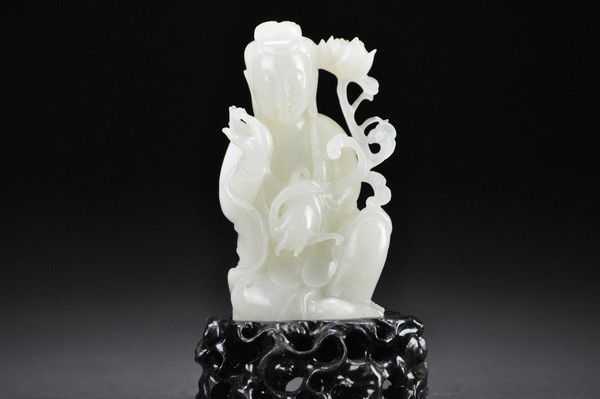 A WHITE JADE CARVING OF GUANYIN.: - A WHITE JADE CARVING OF GUANYIN. holding a peony stem bearing blossom,wearing long layered robes falling in graceful folds and a scarf draped around the back and over the arms,the hair drawn up into