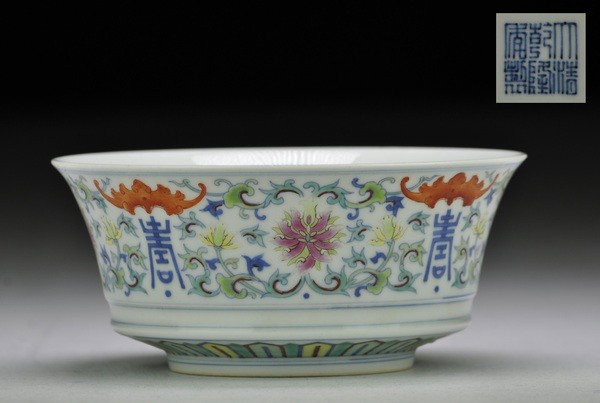 AN UNUSUAL DOU CAI BOWL.(MARK OF QIANLONG): The upright sides sharply angled above the tapering ring foot and flaring towards the rim,the exterior painted above a double bow-string band with an iron red bats and lotu scroll.six character mark o