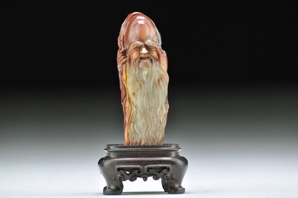 A RED SOAPSTONE CARVING OF SHOULAO.: Shown standed wearing full robe and hold a peach,his facial features well-defined.3 3/4'' H