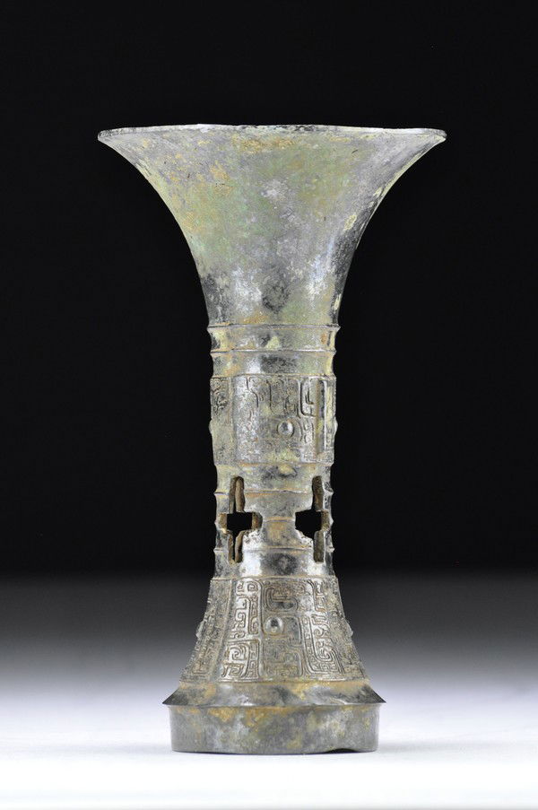 A BRONZE RITUAL WINE VESSEL, GU (SHANG DYNASTY): With plain trumpet-form neck above a pair of bow-string bands, the rounded mid-section flat-cast with a band of two pairs of dragons with rounded eyes centered on a narrow flange and set between narro