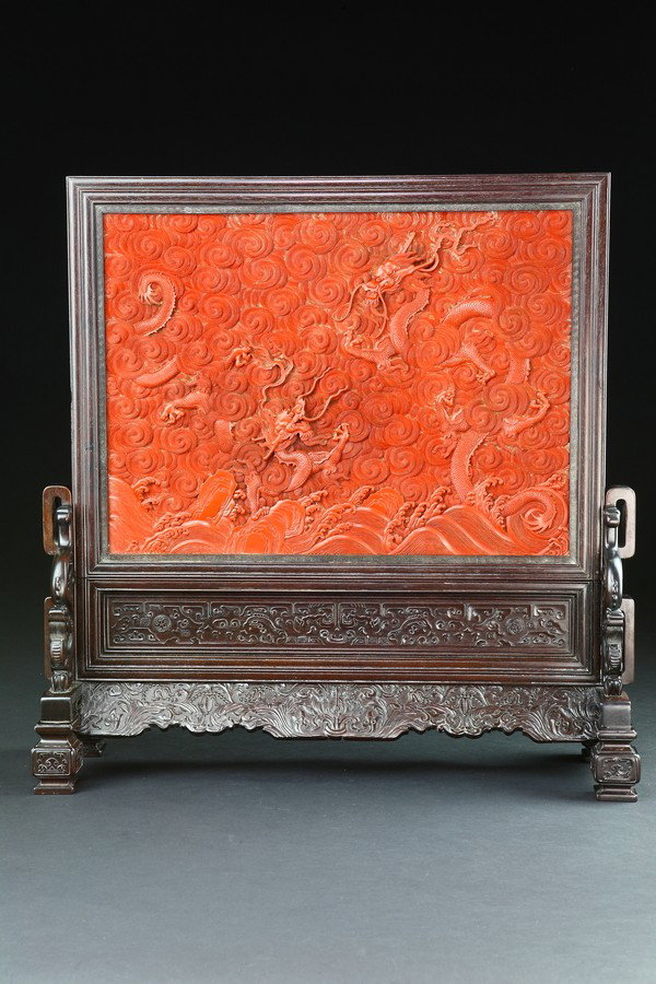 A QIANLONG STYLE ZITAN AND CARVED RED LACQUER TABLE: the red cinnabar lacquer with two three claws dragon striding throught clouds, all reserved on the ochre lacquer ground and set into the zitan base carved on the aprons with bats amidst clouds, suppor