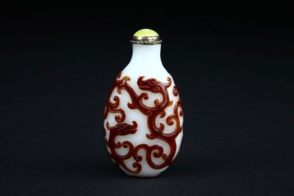 A RED OVERLAY WHITE GLASS SNUFF BOTTLE .(QING DYNAS: Of compressed form with lip and recessed foot surrounded by a footrim, carved through the ruby-red overlay on either side with a writhing chi dragon and its young, 2 3/8''H