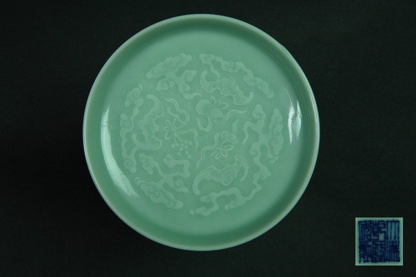 A CARVED CELADON GLAZED DISH .(MARK AND PERIOD OF : The rounded sides flaring slightly towards the rim, the interior carved with four bats in flight between clouds, covered inside and out with a glaze of very pale blue-green tone.1 3/8''H 4 3/8''Diam