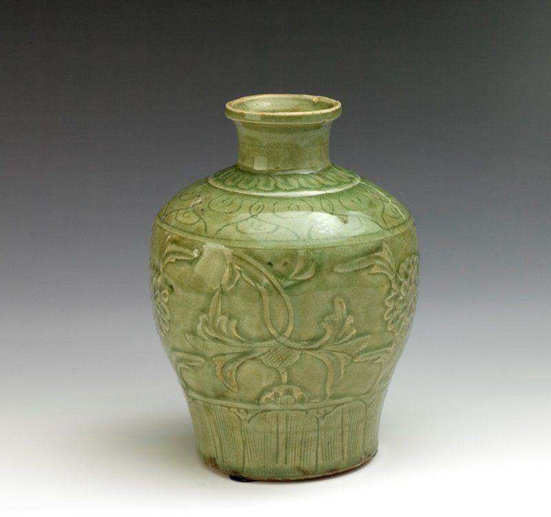 A carved celadon glazed vase, Ming Dynasty: Ming Dynasty The elongated ovoid body fluidly carved with leafy peony scroll within cloud bands above and below, with a petal border encircling the base H: 7 5/8 in Diam: 5 1/2 in