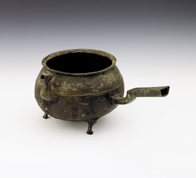A Chinese bronze ritual pouring vessel, Han Dynast: Han Dynasty raised on three short legs with lion masks , silver wire inlaid pattern designs to the body Diam: 7 1/2 in H: 5 7/8 in x L: 12 3/4 in