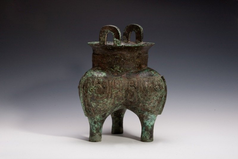 A bronze tripod ritual food vessel.Ding , SHANG/ZH: SHANG/ZHOU DYNASTY Bronze and green tone, with decaying surface and adorned with imperial design. Three legged stand and two N- shaped handles. On the inner rim of the item has small carving. 10 3/4''