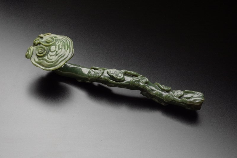 A spinach jade ruyi scepter, QING DYNASTY: QING DYNASTY Spinach- green colour, decorated with cloud- like design on the head and body. 13 1/2'' long