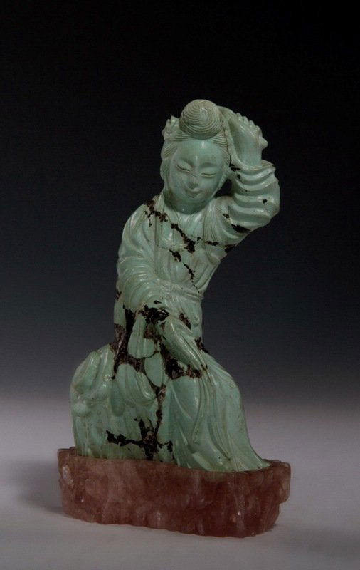 A carved turquoise beauty and stand, REPUBLIC PERI: REPUBLIC PERIOD Beauty is sea- green turquoise colour, figure is erected with left hand holding her hand and right hand on her left leg. Displayed on a pink crystal stand. 6 7/8'' tall with stand